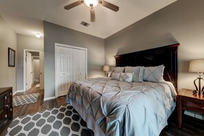Un dormitorio con una cama grande, un ventilador de techo, una mesita de noche y una lámpara.