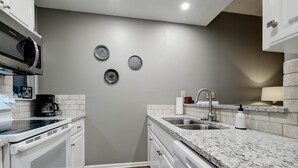 Eine moderne Küche mit weißen Schränken, Granit Arbeitsplatten, einer Edelstahl-Spüle und einer Mikrowelle.