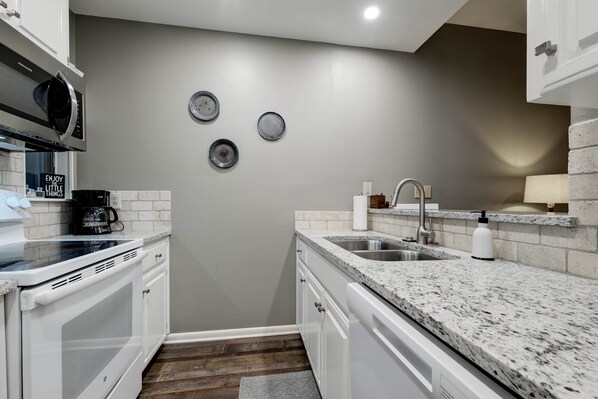 A modern kitchen with white cabinetry, granite countertops, a stainless steel sink, and a microwave.