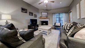 Ein Wohnzimmer mit Kamin, Deckenventilator und Fernseher.