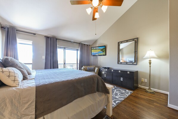 A bedroom with a bed, a dresser, a desk, a lamp, a ceiling fan, and a window.
