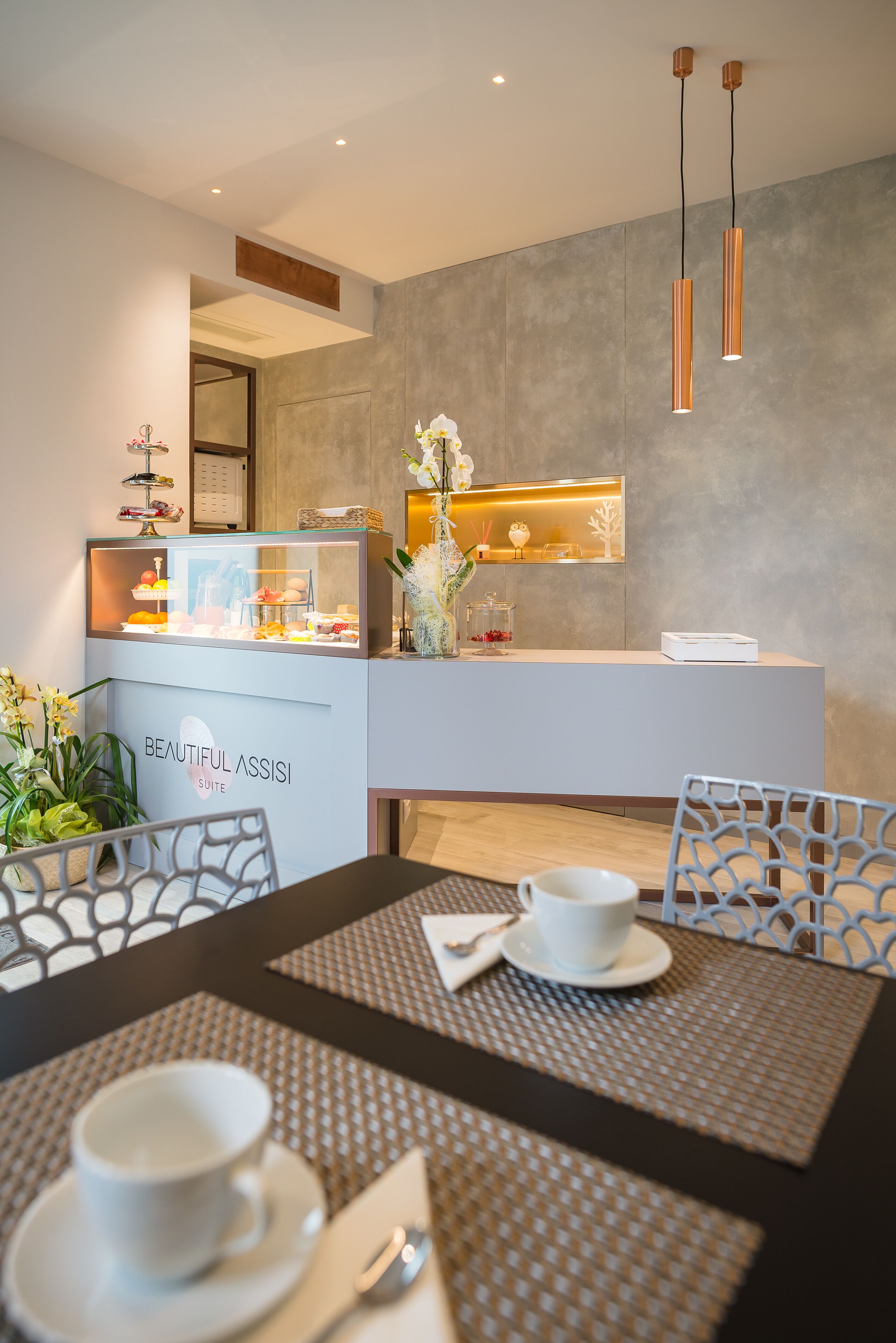 Una moderna area reception hotel con un bancone che espone servizi, un’area salotto con tavoli e sedie, e un arredamento dallo stile minimalista.