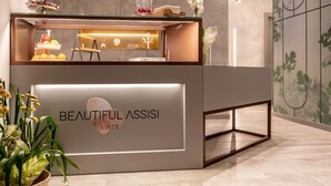 A reception desk with a glass top, a sign reading "BEAUTIFUL ASSISI SUITE", and a potted plant to the left. - Beautiful Assisi Suite (Assisi)