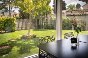 Blick aus einem Fenster auf einen gepflegten Garten mit Rasen, Holzzaun und einem Tisch mit Stühlen.