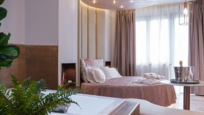 A modern hotel room with a large bed, a seating area, a small table with a bottle and glasses, and a large plant. - Beautiful Assisi Suite (Assisi)