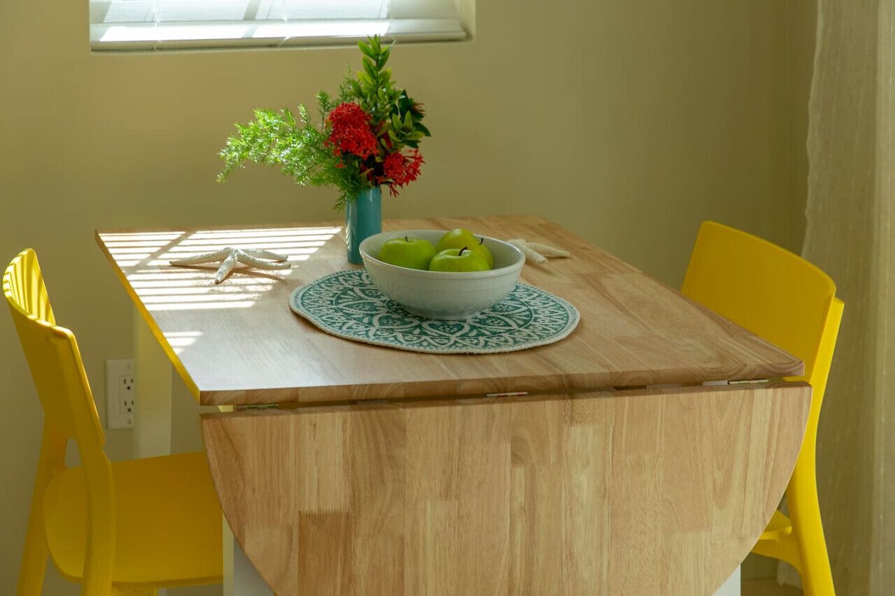 A dining table with a bowl of green apples, a vase with flowers, and yellow chairs.