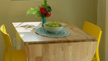 A dining table with a bowl of green apples, a vase with flowers, and yellow chairs.