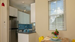 A compact kitchen with a stainless steel refrigerator, a blue tiled backsplash, and a dining area with a wooden table and yellow chairs.