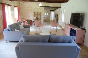 A modern living room with a grey sofa, two pink chairs, a small white table, and a pink cabinet with a TV.