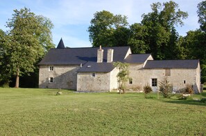 A stone building with a sloped roof and chimneys, surrounded by a grassy lawn and trees.