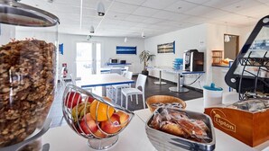 Een moderne kantoorruimte met een grote tafel voor het ontbijt, een fruitschaal, een broodtrommel en een koffieapparaat.