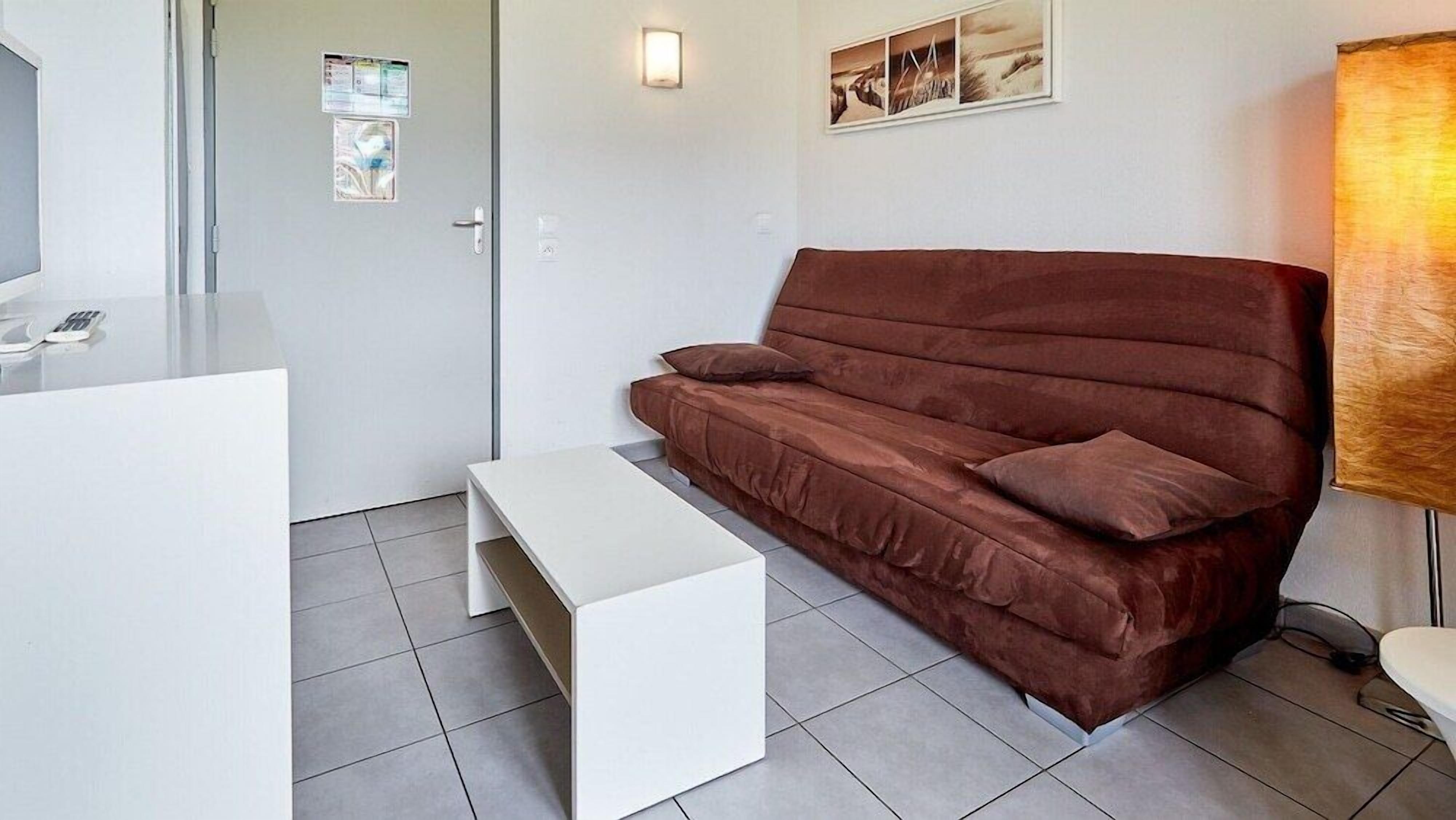 Quarto moderno com um sofá marrom, uma mesa de centro branca e uma pequena mesa branca.