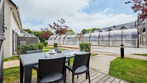 Een terras met een tafel en stoelen, een kasconstructie en een woongebouw.