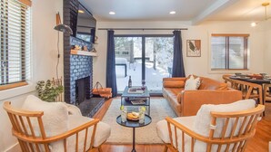 A cozy living room with a fireplace, a sofa, two armchairs, a coffee table, and a dining area with a table and chairs. - Andora Villa #123 Newly Remodeled 2 BR / 2Bath, Centrally Located, Close to Town Center (Ketchum)