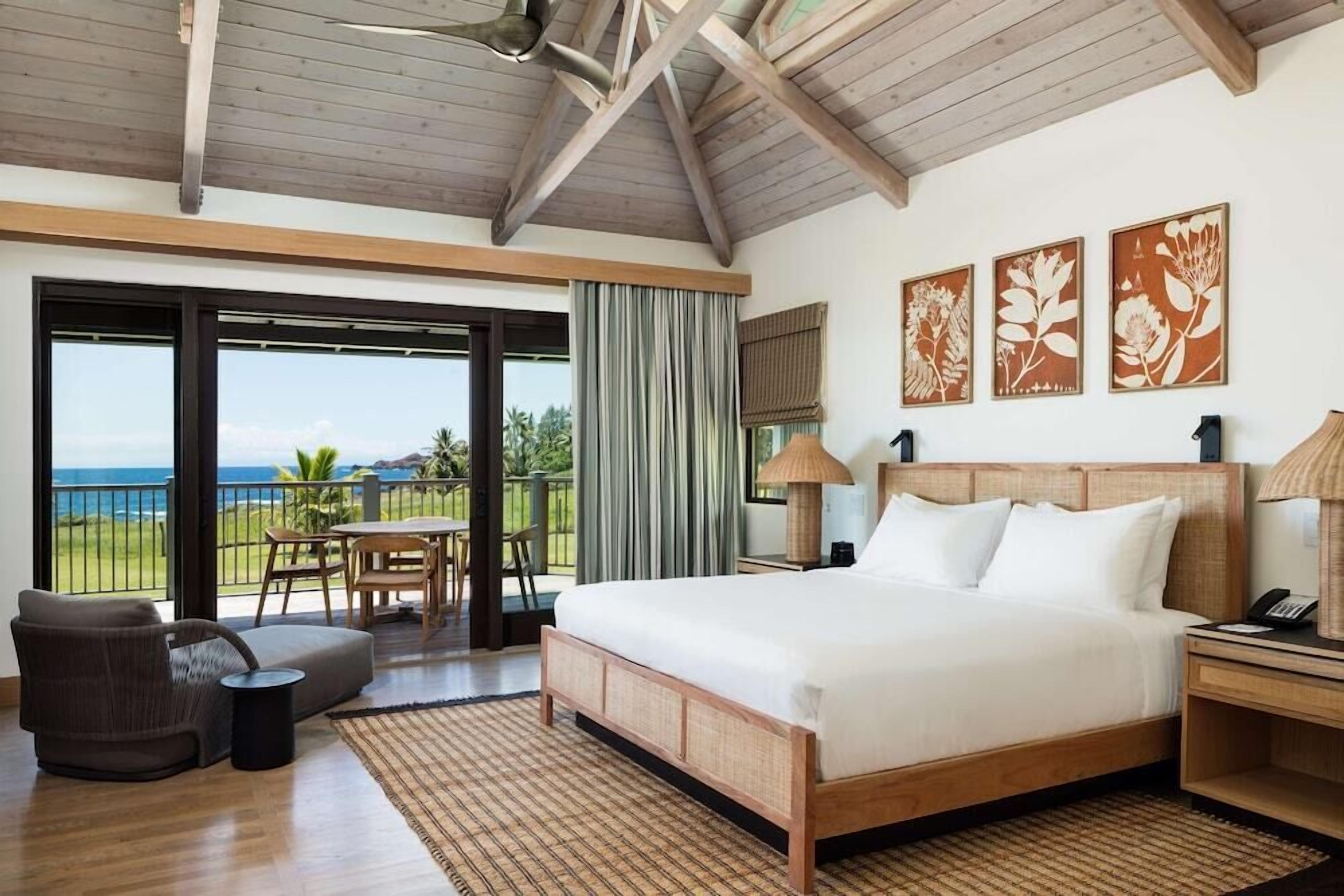 Un'ampia camera da letto con un grande letto, un balcone vista oceano e un'area pranzo con tavolo e sedie.