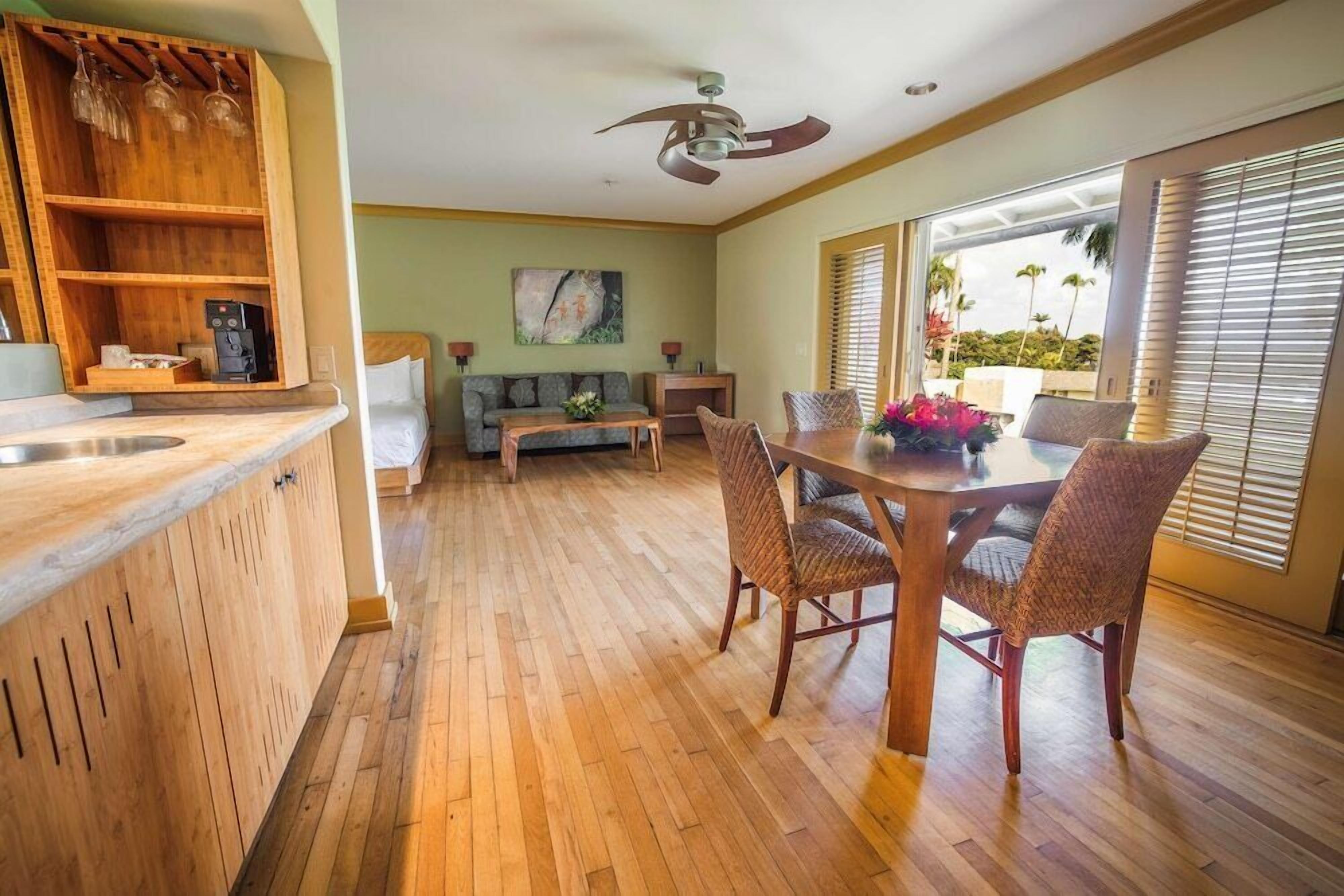 A spacious living area with a wooden floor, a dining table with chairs, a sofa, and a coffee station.