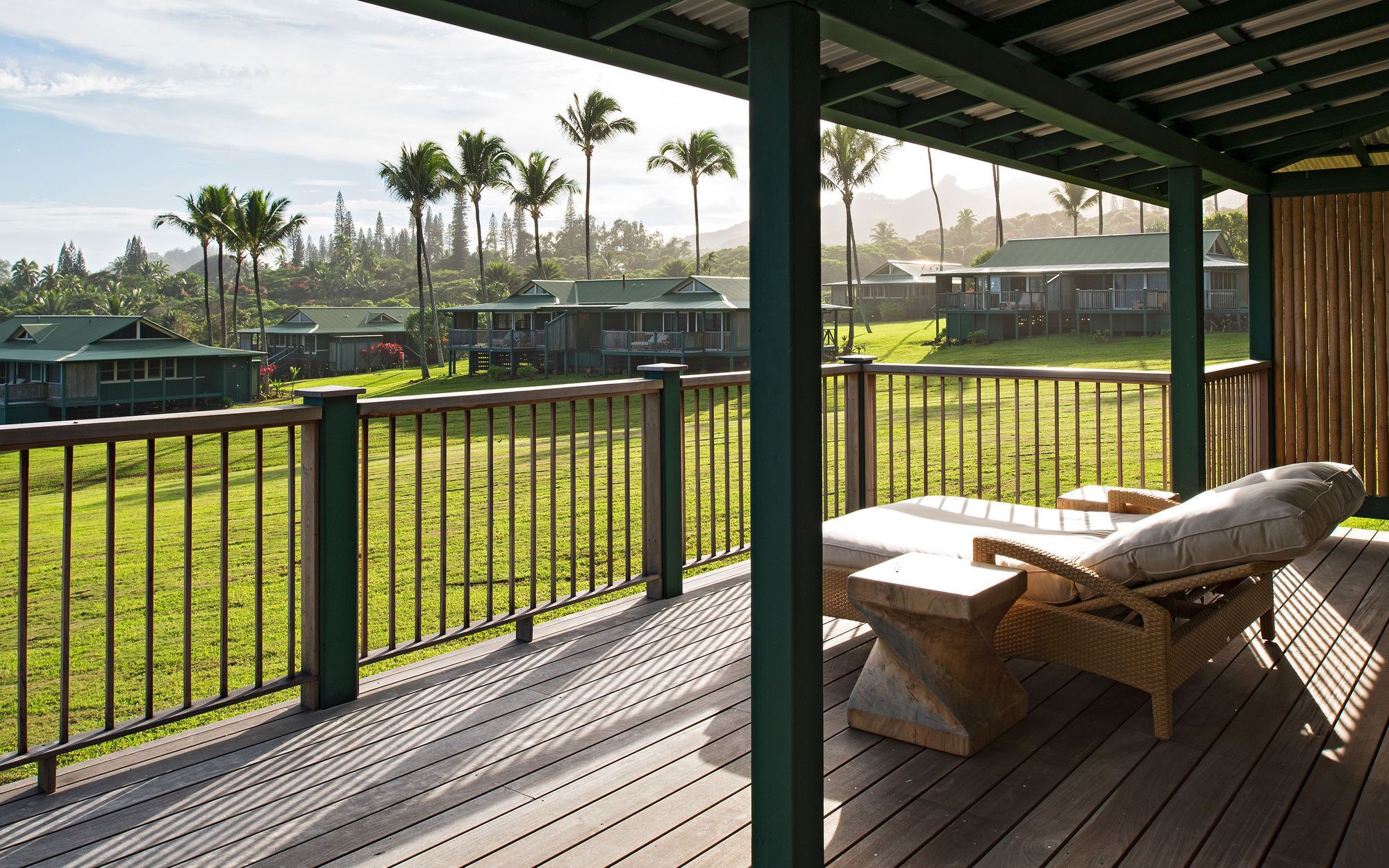 A wooden deck with a view of a well-maintained lawn and several buildings in the background.