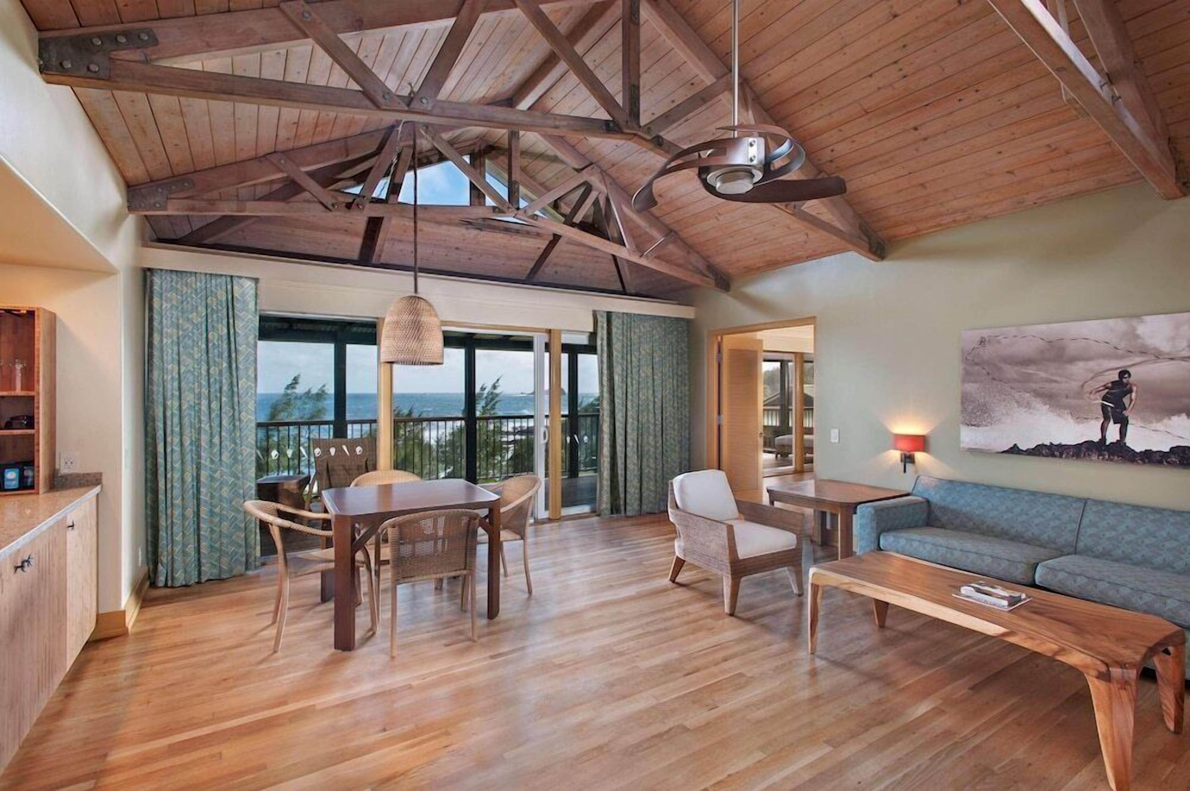 A spacious living area with a wooden ceiling, a dining table with chairs, a sofa, and a painting on the wall.