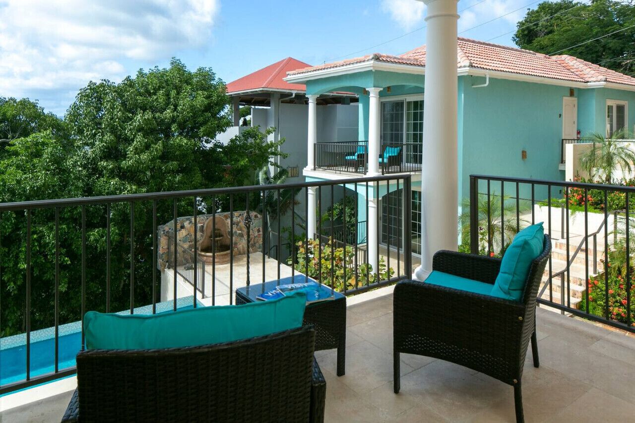 A balcony with wicker furniture and a view of a house with a red roof.