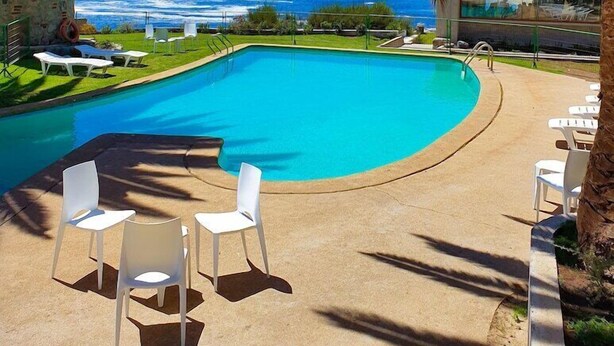 Une piscine avec vue sur l’océan, entourée de palmiers et de chaises blanches.