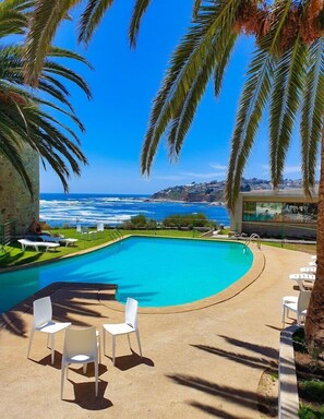 Una piscina con vista al océano, rodeada de palmeras y sillas blancas.