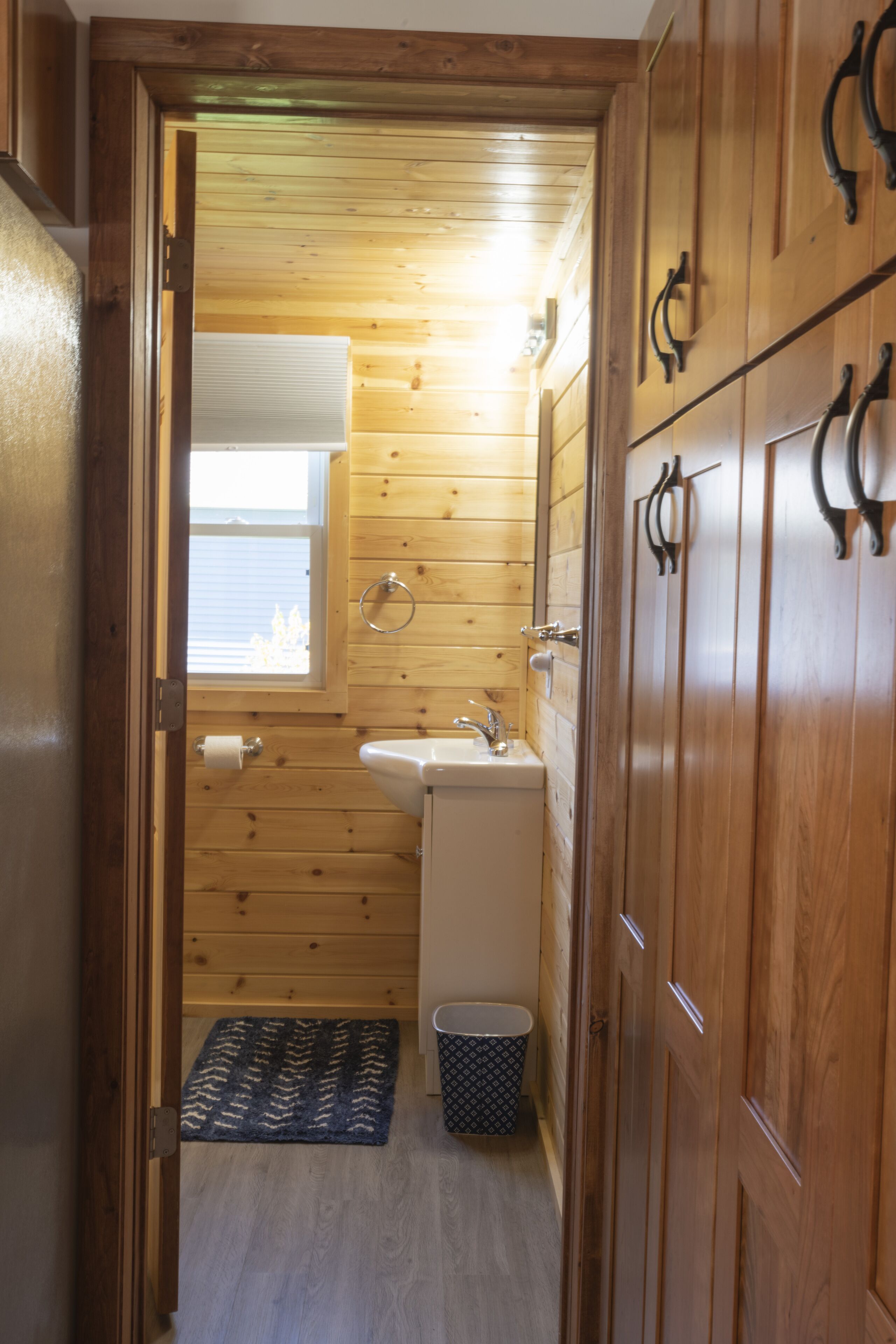 A narrow wooden bathroom with a sink, toilet, and a small window.