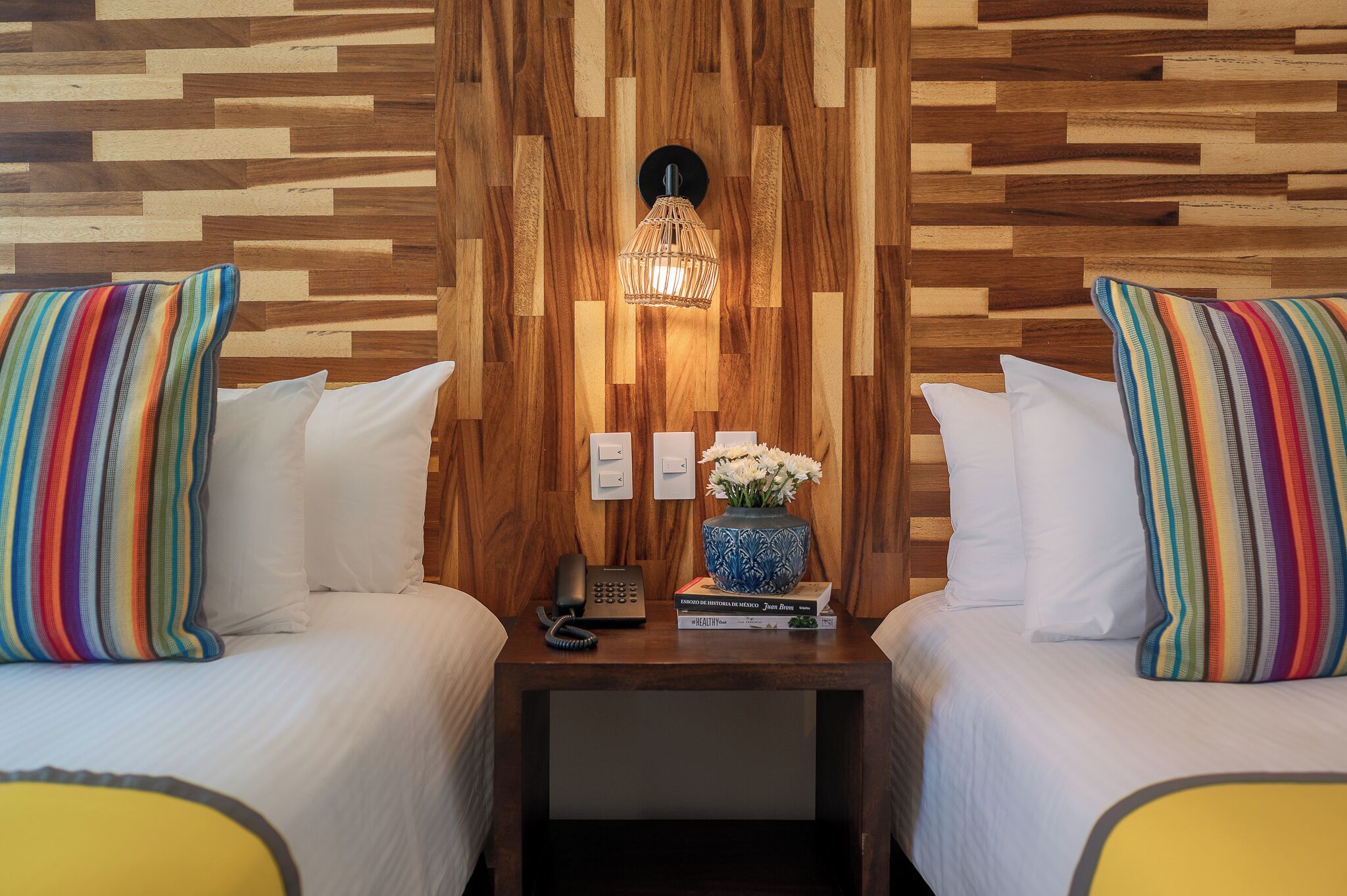 A hotel room with two beds, a nightstand, a telephone, a vase with flowers, and a wall with a wooden pattern.