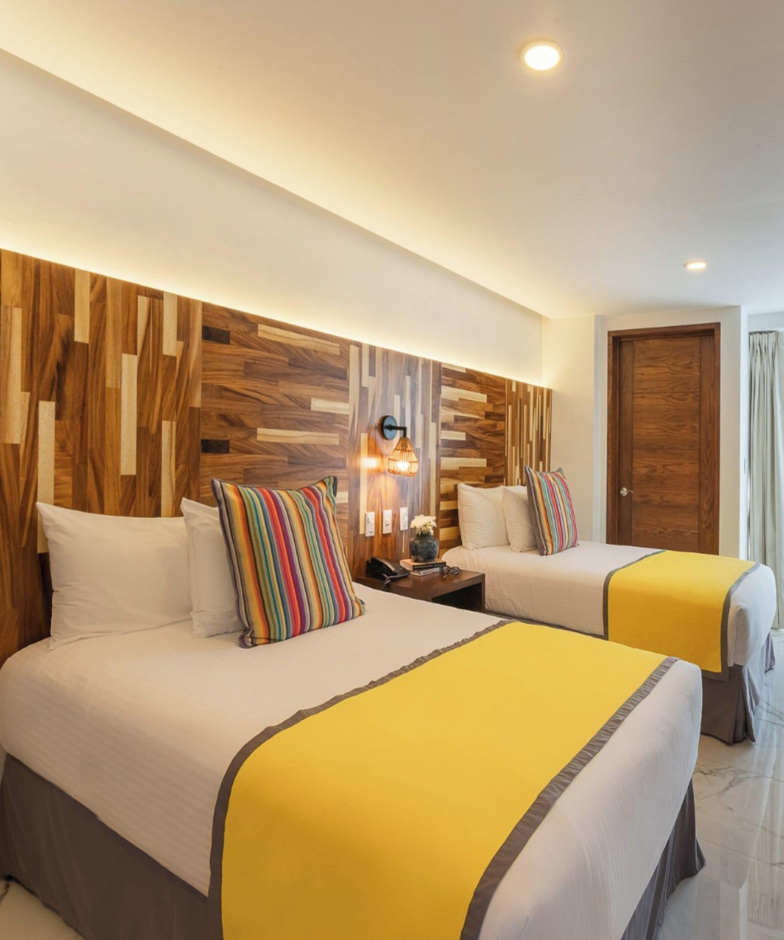 Een hotelkamer met twee bedden, paneel hoofdbord, een nachtkastje met lamp en een deur.