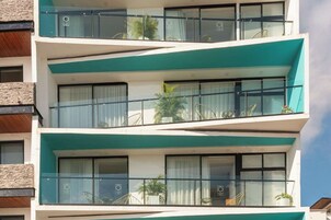 Un edificio de varios pisos con balcones, ventanas grandes y algunas plantas en macetas.
