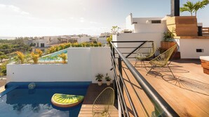 A rooftop pool area with a clear view of the cityscape, surrounded by potted plants and modern outdoor furniture.