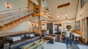 Un vaste espace de vie agrémenté d’un escalier en bois, de canapés en cuir, d’une table à manger et d’une cuisine située au fond de la pièce.