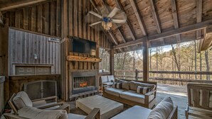 L’intérieur chaleureux d’un chalet avec une cheminée, des meubles en bois et une grande fenêtre donnant sur une forêt.