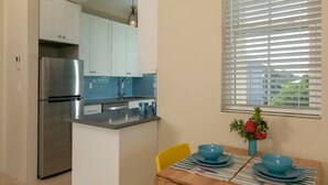 A modern kitchen with white cabinets, a stainless steel refrigerator, and a blue backsplash. There is a dining table with blue plates and a vase of flowers. - Allamanda 3 - 1 bedroom suite at Seagrape Vista (Cruz Bay)