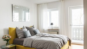 Een slaapkamer met een bed, nachtkastje, lamp, raam en balkon.