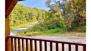 A wooden deck overlooking a forested area with a road. - 2-bedroom vacation home just 10 minutes from Viroqua's charming downtown (Viroqua)