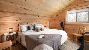 A cozy wooden cabin bedroom with a bed, bedside tables, a chair, and a window. - 2-bedroom vacation home just 10 minutes from Viroqua's charming downtown (Viroqua)
