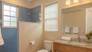 Une salle de bain avec des toilettes, un lavabo et un miroir. Des serviettes sont accrochées au mur et il y a une fenêtre avec des stores.