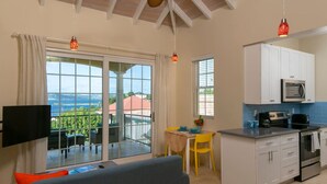 Un salon moderne comprenant un canapé, une table à manger avec des chaises, un coin cuisine avec des placards et des appareils électroménagers, et un balcon avec vue.