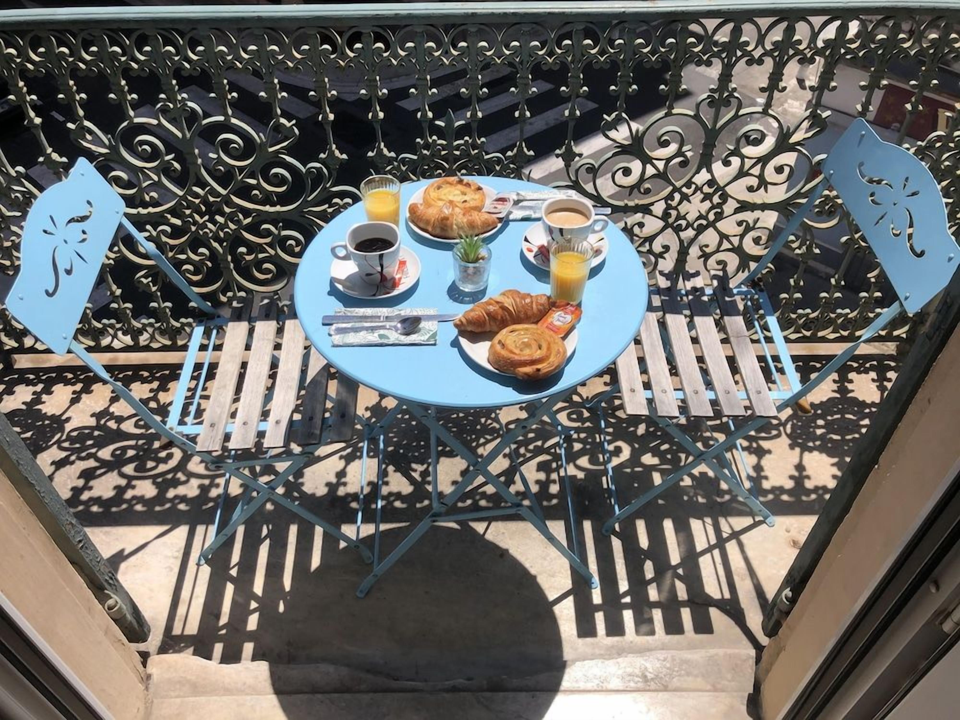 Una mesa redonda cubierta con un mantel azul, un croissant, un vaso de jugo de naranja, una taza de café y una pequeña planta.