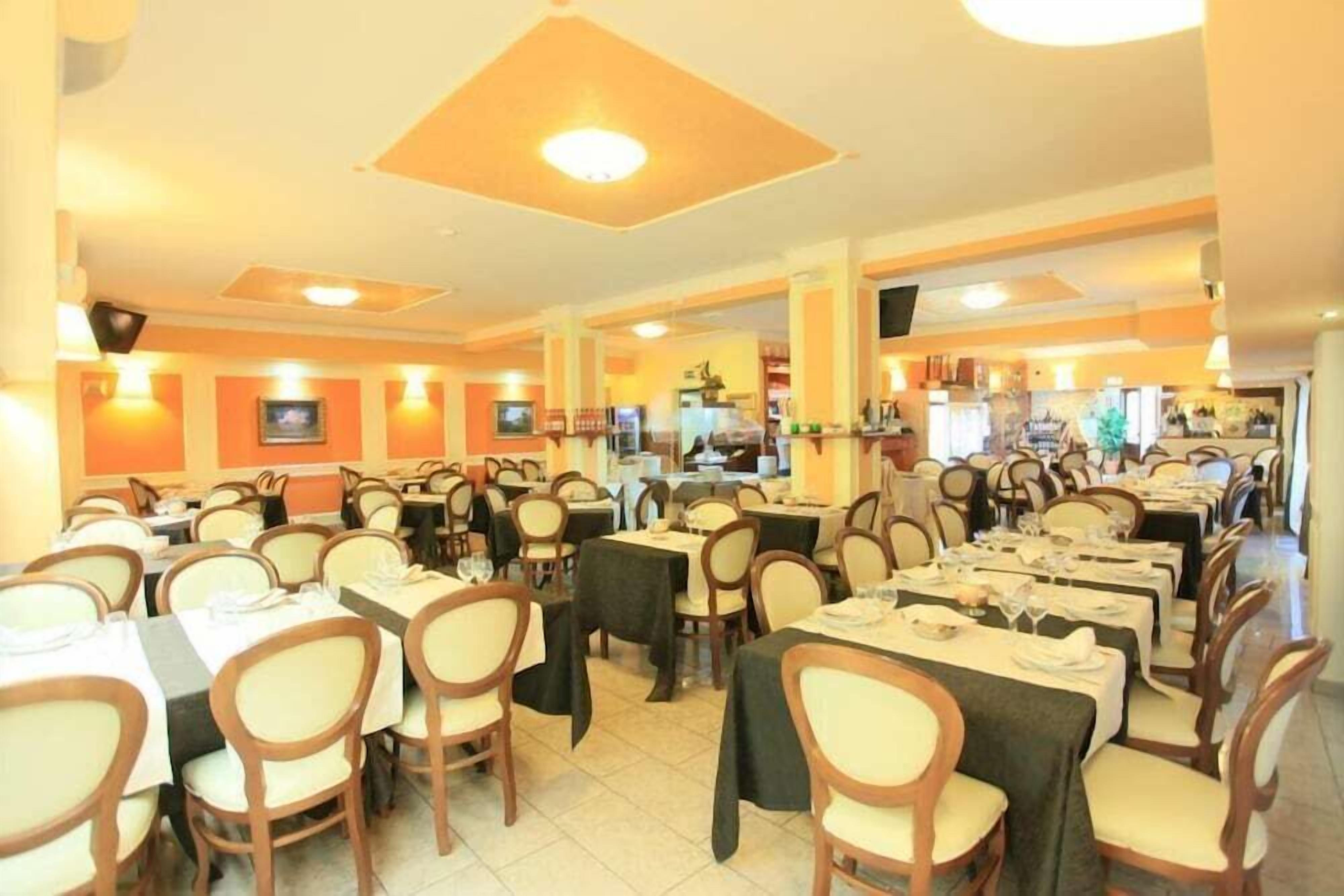 Un restaurante con varias mesas y sillas, un área de cocina al fondo y un techo con iluminación empotrada.