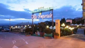 L'ingresso di un hotel con un cartello che riporta la scritta "SALA RICEMIENTE Villa Imperiale" e un'area di parcheggio con frecce direzionali.