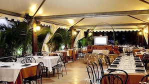 Un restaurante al aire libre con mesas dispuestas para comer, rodeado de follaje y una estructura tipo carpa.