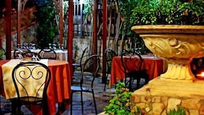Un espacio exterior con mesas y sillas, una jardinera de piedra con una vela y follaje.