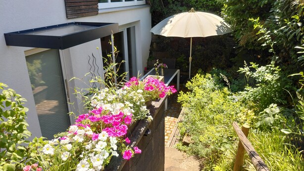 A garden with a variety of flowers, a wooden fence, and a house with a window and a door. - Ferienwohnung Boger (Wannweil)
