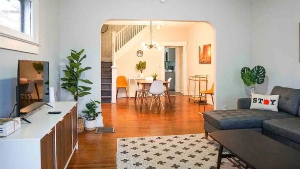 Uma sala de estar moderna com sofá, mesa de centro e área de jantar com cadeiras e mesa. Há uma escada que leva a outro cômodo.