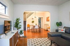 Una sala de estar moderna con sofá, una mesa de centro y un comedor con sillas y una mesa. Se ve una escalera que sube a otra habitación.