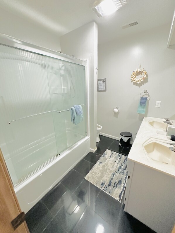 Une salle de bain moderne avec une douche à parois de verre, des toilettes et un coin lavabo agrémenté d’un porte-serviettes et d’une couronne décorative.