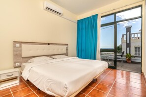 Una camera da letto con un letto, un comodino, un condizionatore, un balcone con vista sul mare e una pianta in vaso.