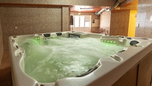 A hot tub with green lighting, a wooden floor, and a tiled wall.