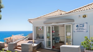 A coastal building with a tiled roof, a glass door entrance, and a sign indicating a place for sale.